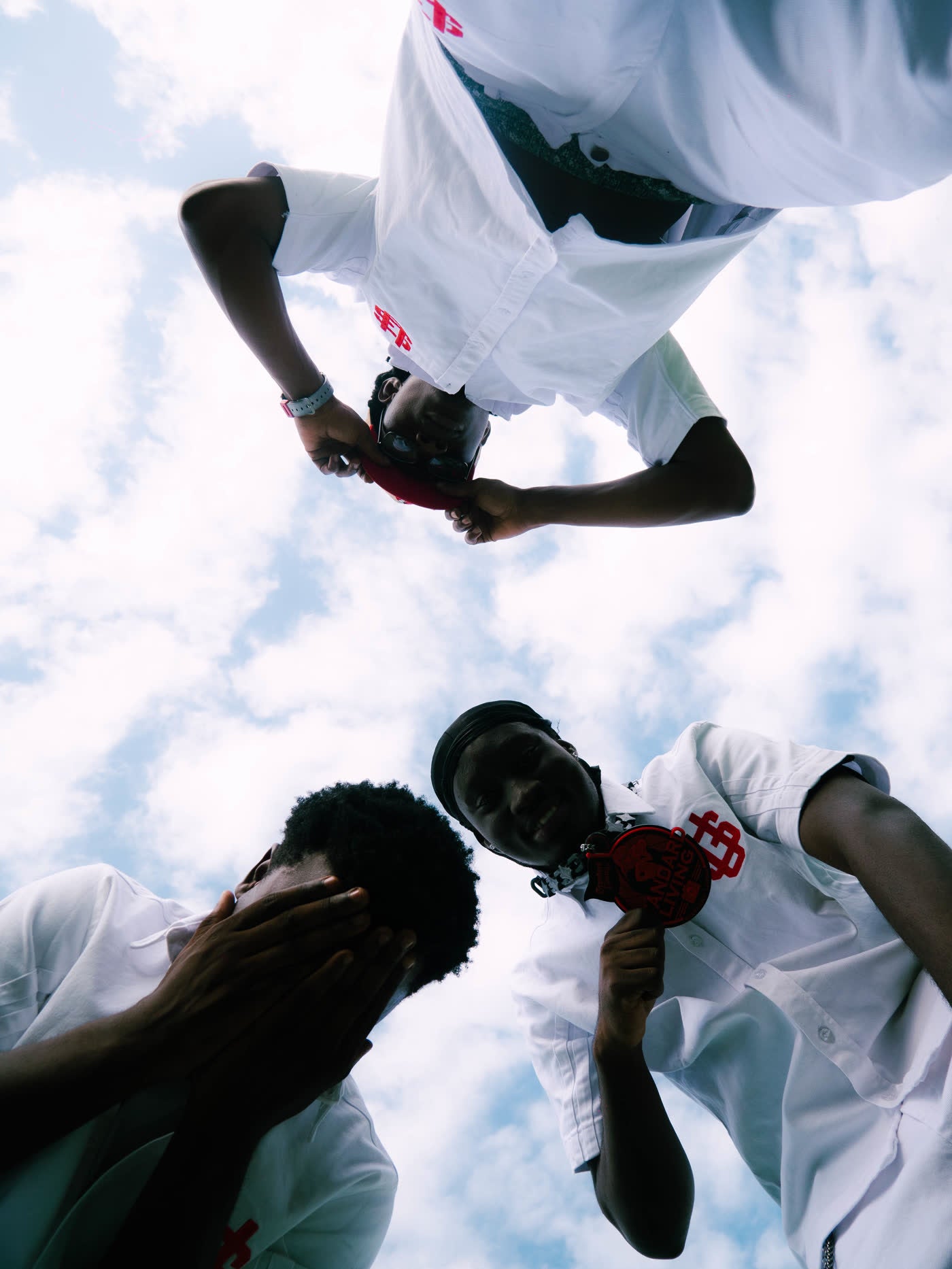 Low angle shot of models in white tees leaning over the camera against a blue sky