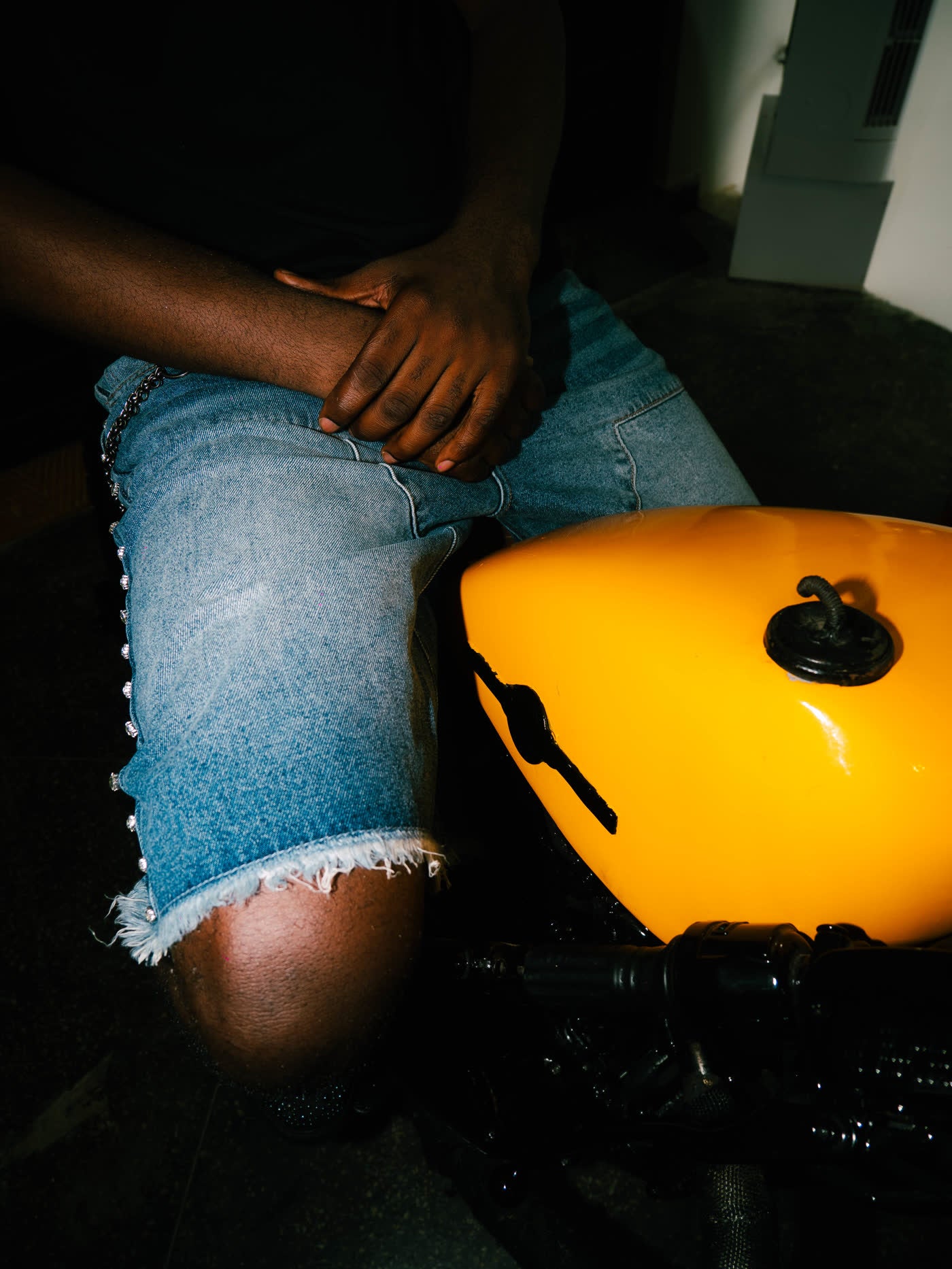 Close detail of hands on the seat of a yellow motorcycle above a frayed denim hem